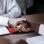 two people shaking hands over a desk with documents